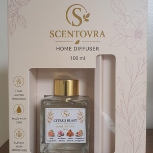 May include: A Scentovra 100 ml home diffuser set in a cream-colored box with floral illustrations. The square glass bottle features a gold cap and a label reading Citrus Blast, listing scents like Pink Grapefruit, Sea Salt, Orchid, and Mangosteen.