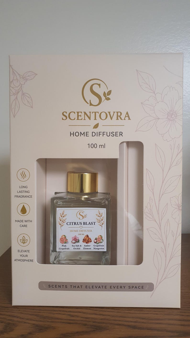 May include: A Scentovra 100 ml home diffuser set in a cream-colored box with floral illustrations. The square glass bottle features a gold cap and a label reading Citrus Blast, listing scents like Pink Grapefruit, Sea Salt, Orchid, and Mangosteen.