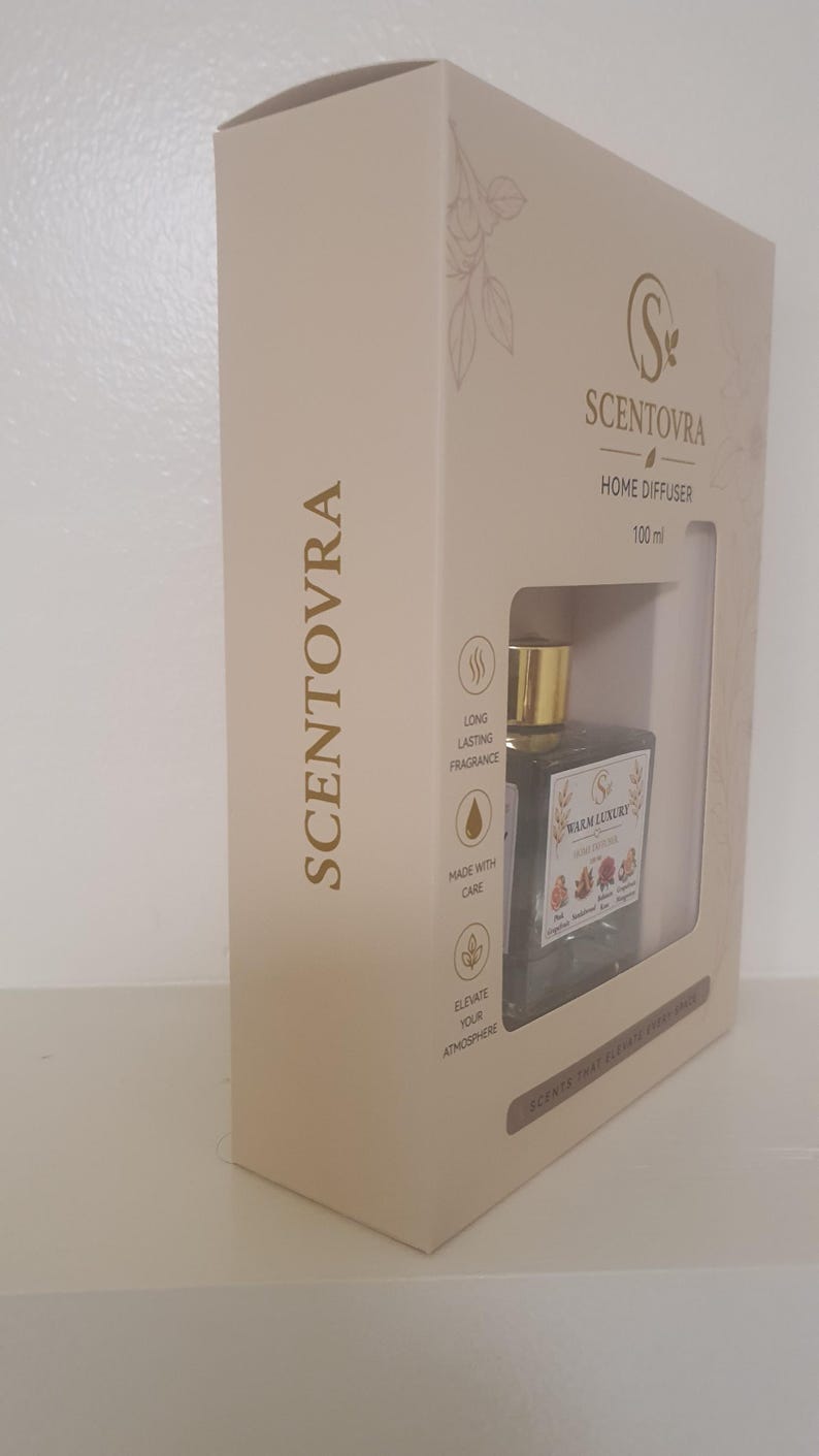 May include: A beige rectangular box for a Scentovra home diffuser containing a 100 ml glass bottle with a gold cap. The packaging features the brand name, icons for long-lasting fragrance, made with care, and elevate your atmosphere, and a label reading Warm Luxury.