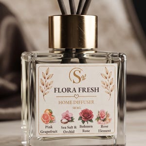 May include: A clear square glass home diffuser bottle with a gold cap and black reed sticks. The label reads Flora Fresh Home Diffuser 50 ml, featuring illustrations of pink grapefruit, sea salt and orchid, Bohmen rose, and rose element.