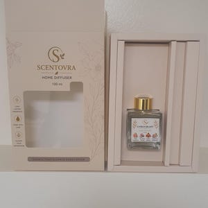 May include: A Scentovra 100 ml home diffuser set in a light beige box. The square glass bottle has a gold cap and a label reading Citrus Blast with illustrations of pink grapefruit, sea salt, orchid, amber, and tangerine. The box features floral line art.