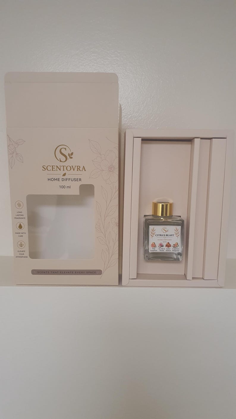 May include: A Scentovra 100 ml home diffuser set in a light beige box. The square glass bottle has a gold cap and a label reading Citrus Blast with illustrations of pink grapefruit, sea salt, orchid, amber, and tangerine. The box features floral line art.