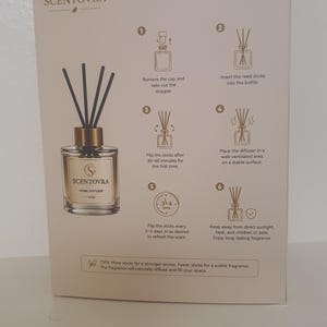 May include: A rectangular product box for a Scentovra home diffuser featuring a clear glass bottle with a gold cap and black reed sticks. The box displays instructions titled HOW TO USE? with six numbered steps and text explaining the process.
