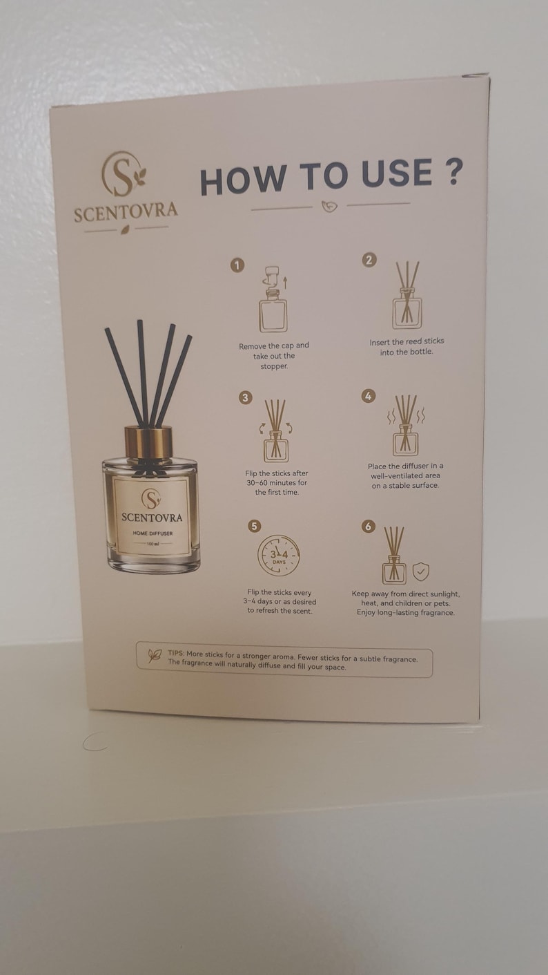 May include: A rectangular product box for a Scentovra home diffuser featuring a clear glass bottle with a gold cap and black reed sticks. The box displays instructions titled HOW TO USE? with six numbered steps and text explaining the process.