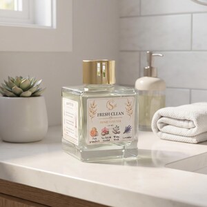 May include: A square glass home diffuser bottle with a gold cap and a label reading FRESH CLEAN HOME DIFFUSER 100 ML. The label features illustrations of pink grapefruit, sea salt, orchid, white birch, and lavender. The bottle contains clear liquid.