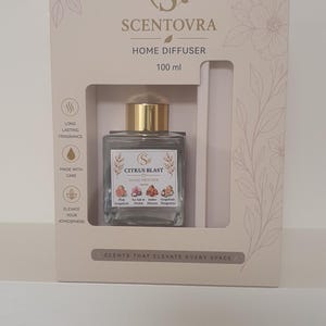 May include: A Scentovra Citrus Blast home diffuser set in a beige box with floral line art. The square glass bottle has a gold cap and a label listing Pink Grapefruit, Sea Salt & Amber, Orchid Element, and Mangosteen. The box states 100 ml.
