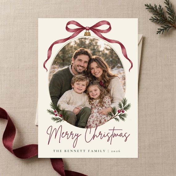Card front with a family photo in an ornament frame under a cranberry watercolor bow, reading Merry Christmas