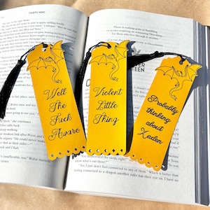 May include: Three rectangular yellow bookmarks with black dragon illustrations and black tassels. The bookmarks feature the text: Well The Fuck Aware, Violent Little Thing, and Probably thinking about Xaden, each with a scalloped bottom edge.