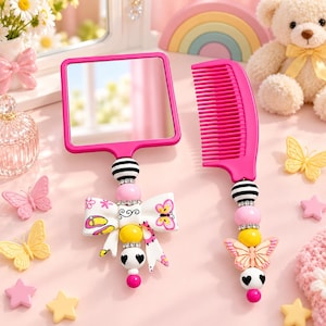 May include: A square hand mirror and a hair comb, both featuring handles decorated with colourful beads, rhinestones, and a white bow with butterfly and flip-flop patterns. The mirror and comb are bright pink with black, white, and yellow accents.