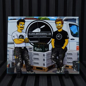 Op de afbeelding: Een rechthoekige glazen plaat met een cartoonillustratie van twee werkers voor een witte bestelwagen. De tekst luidt KAKELBRÖDERNA AB KAKE & KLINKER. De afbeelding toont stapels dozen met het label KAKEL, een krat Carlsberg-bier en diverse gereedschappen.
