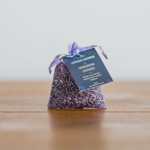 May include: A small purple bag filled with dried lavender flowers. The bag has a white tag that reads "Lothian Lavender Homegrown Lavender Grown in our Cottage Garden in East Lothian Scotland www.lothianlavender.co.uk By Kat"