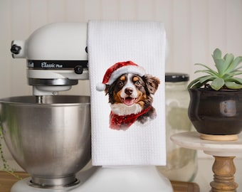 May include: White kitchen towel with a colorful illustration of a Bernese Mountain Dog wearing a Santa hat. The dog is smiling and has a red and white scarf around its neck.