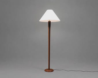 May include: A floor lamp featuring a tall, slender, dark brown wooden stand with a smooth, tapered profile. The lamp is topped with a white, conical fabric shade that flares outward, supported by a circular wooden base on the floor.