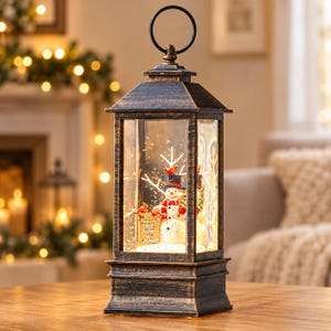 May include: A rectangular lantern with a distressed bronze finish and a top ring handle. Inside, a snowman wearing a black top hat and red scarf stands next to a sign that reads Frosty's Tree Farm and Firewood, surrounded by white branches.