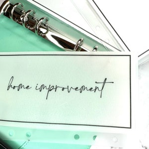 Puede incluir: Una agenda de cuero verde claro con un encuadernador de anillos de plata y un protector de p&aacute;gina de pl&aacute;stico transparente con el texto "home improvement" escrito en negro.