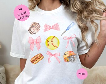 May include: White t-shirt with a softball theme. The shirt features a softball, bat, glove, hot dog, and bows. The text "WHITE" is printed on the bottom right corner of the shirt.
