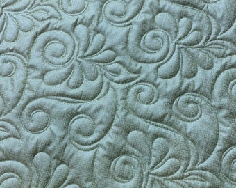 May include: A close-up of a light green fabric with a quilted pattern of swirling leaves and vines.