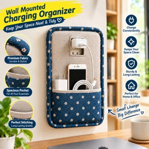 May include: A wall-mounted charging organiser featuring a rectangular beige fabric panel with a dark blue floral pocket. The organiser includes a cutout for a wall outlet, a white power adapter, a smartphone, and a coiled white charging cable.