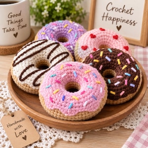 Puede incluir: Una colección de cinco rosquillas de ganchillo en un cuenco de madera. Las rosquillas presentan varios colores, incluidos morado, rosa, marrón y crema, decoradas con chispas de lana, formas de corazón y patrones de glaseado.
