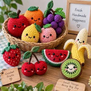 May include: A collection of crocheted fruits with embroidered faces, including a red apple, orange, purple grapes, yellow pear, pink peach, red strawberry, red cherries, watermelon slice, banana, and kiwi, arranged in a woven basket with signs.