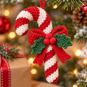 Può includere: Un ornamento a forma di bastoncino di zucchero all'uncinetto con strisce diagonali rosse e bianche. L'ornamento è decorato con un fiocco rosso all'uncinetto, tre piccole bacche rosse all'uncinetto e due foglie di agrifoglio verdi al centro.