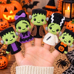 May include: A set of five crocheted finger puppets featuring Halloween-themed characters. The puppets include three green-skinned monsters with black hair, a green-skinned character with a purple dress and bow, and a green-skinned character in a white dress.