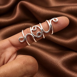 May include: A silver-colored metal ring featuring a long, multi-band design that wraps around the finger. The center of the ring displays the Cancer zodiac symbol, characterized by two circular shapes with curved lines, flanked by spiral ends.