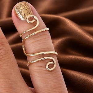 May include: A gold-toned wire finger ring featuring a continuous spiral design that wraps around the finger. The metal wire forms two distinct circular loops at the top and bottom ends, creating an open, adjustable, and lightweight structure.