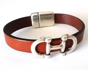 Pode incluir: Um bracelete de couro castanho com um fecho magnético prateado e um design em forma de ferradura prateado.