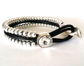 May include: A silver beaded bracelet with a black leather strap and a crystal button closure.