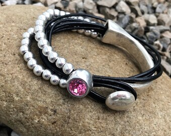 May include: A multi-strand leather bracelet with silver beads and a pink crystal accent. The bracelet has a silver metal clasp and a silver metal charm.