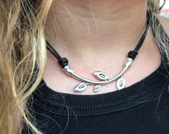 May include: A silver leaf branch pendant necklace on a black leather cord.