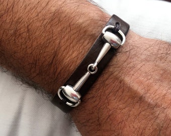 Pode incluir: Um bracelete de couro castanho com um fecho de prata em forma de freio de cavalo.