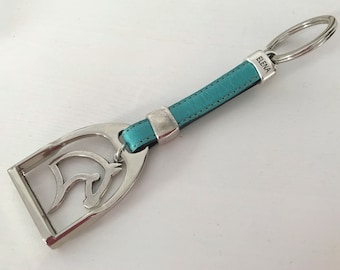 May include: A turquoise leather keyring with a silver horse head charm and a silver key ring. The keyring has the word "ELENA" engraved on it.
