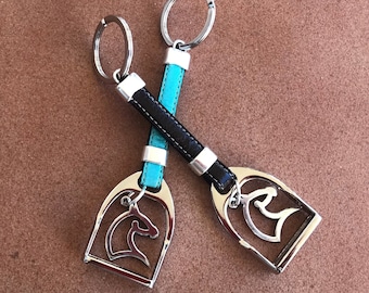 May include: Two silver keychains with leather straps. One strap is turquoise blue and the other is black. Both keychains feature a silver horse head charm.