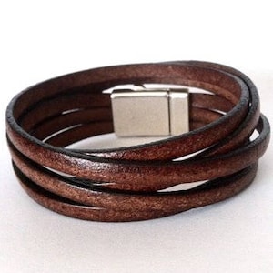 May include: A brown leather bracelet with a silver magnetic clasp. The bracelet is made of multiple strands of leather that are woven together.