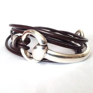 Op de afbeelding: Een bruin lederen armband met een zilveren metalen paardenbit sluiting.