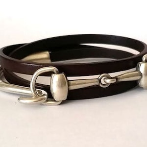 May include: A brown leather wrap bracelet with a silver equestrian bit clasp.