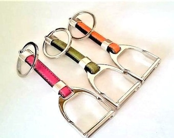 May include: Three stirrup-shaped keychains with leather straps. The keychains are in pink, green, and orange.