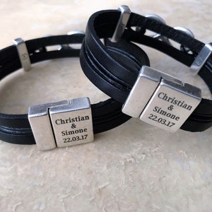 May include: Two black leather bracelets with silver clasps. Each clasp has the text "Christian & Simone 22.03.17" engraved on it.