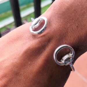 May include: Silver bracelet with two circular links. The links are connected by a small bar. The bracelet is worn on a person's wrist.