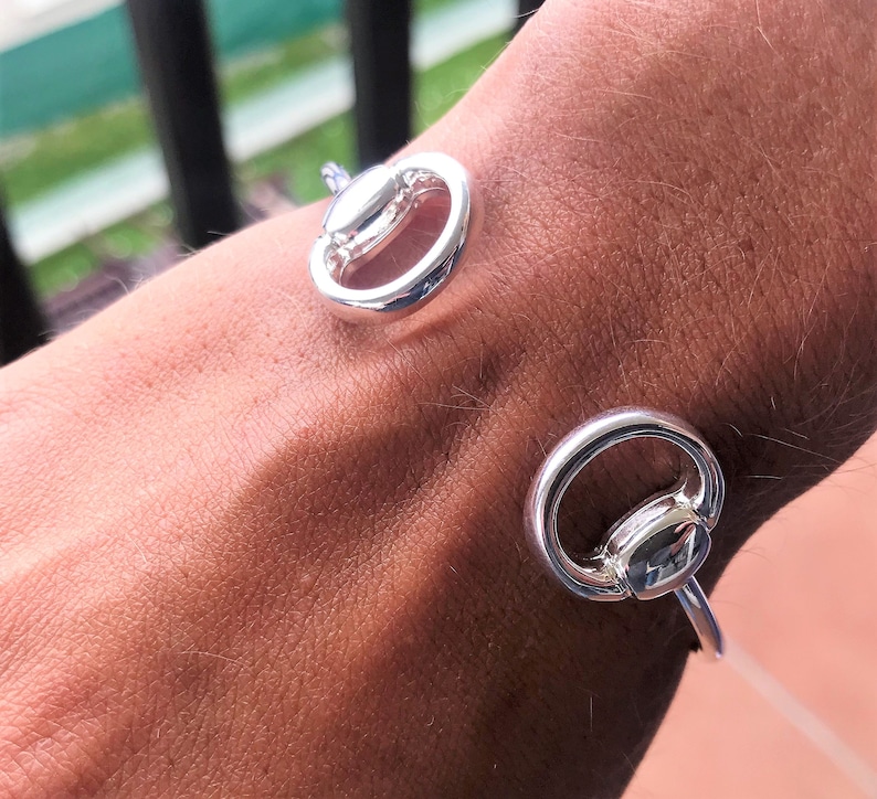 May include: Silver bracelet with two circular links. The links are connected by a small bar. The bracelet is worn on a person's wrist.