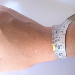 May include: A white measuring tape wrapped around a wrist, showing a measurement of 16 inches.