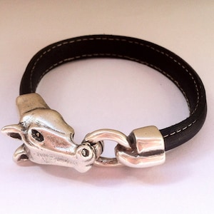Könnte beinhalten: Ein schwarzes Lederarmband mit einem silbernen Pferdekopf-Anhänger und einem silbernen Verschluss.