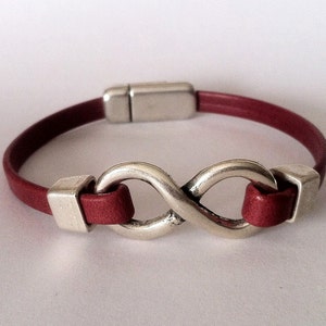 May include: A red leather bracelet with a silver infinity symbol charm. The bracelet has a magnetic clasp.