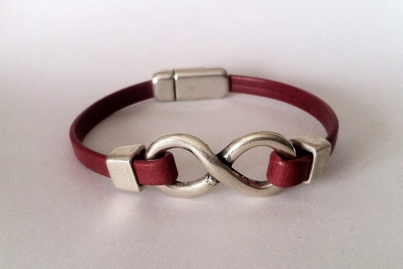 May include: A red leather bracelet with a silver infinity symbol charm. The bracelet has a magnetic clasp.