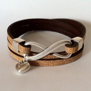 May include: A brown leather wrap bracelet with a silver infinity charm and a small heart pendant.