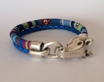 Op de afbeelding: Een blauwe leren armband met een kleurrijk geweven bandje en een zilveren paardenkopgesp.