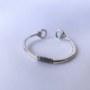 May include: A silver bangle bracelet with a twisted design in the centre and two decorative loops at the ends.