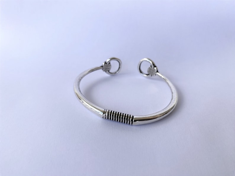 May include: A silver bangle bracelet with a twisted design in the centre and two decorative loops at the ends.